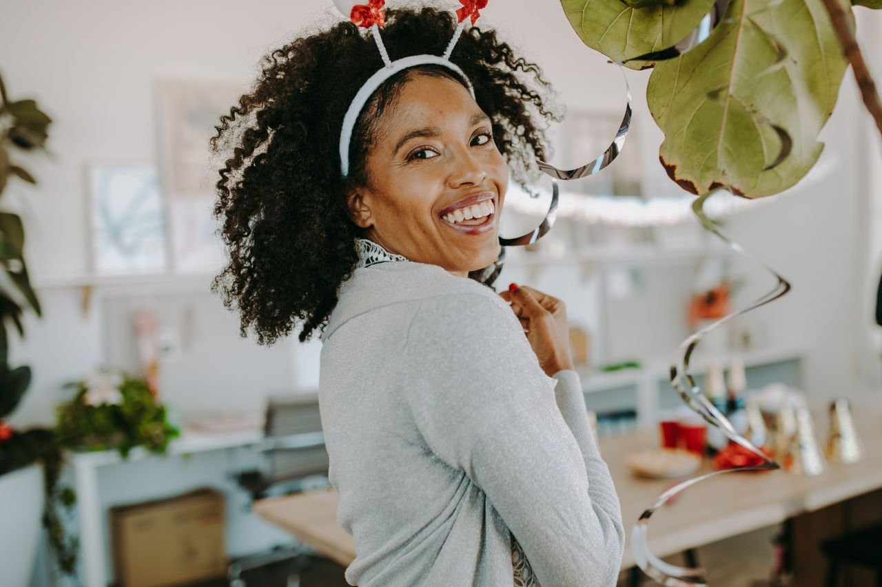 embark Smiling woman enjoying a festive office holiday party with decorations.