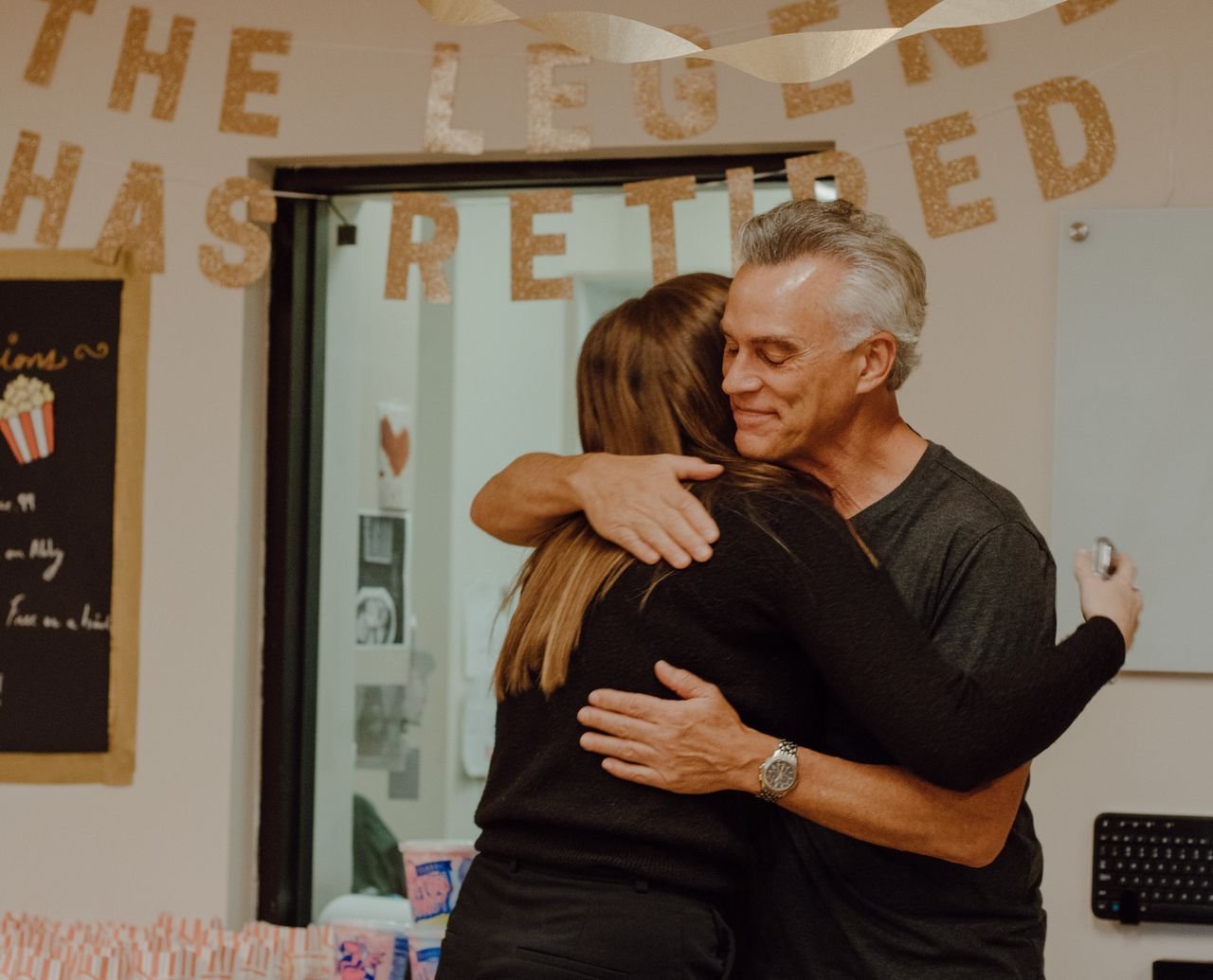 gallery-06 A heartfelt moment as two people embrace at a retirement party with festive decor.